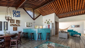 A spacious living area with a kitchen, bar stools, a glass coffee table, and a hammock. - Beira Mar-Cozinheira-Piscina-4QT-SH029 (Sirinhaem)