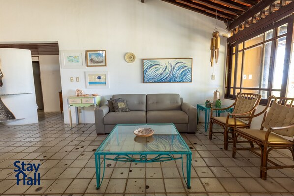 Una sala de estar con una mesa de centro de vidrio, un sofá y dos sillones. Hay cuadros enmarcados en la pared y una ventana con vistas.