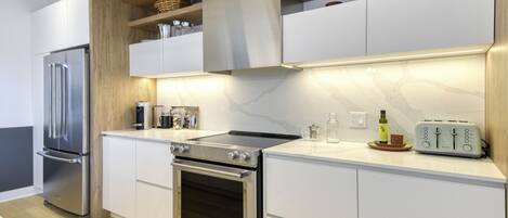 A modern kitchen with stainless steel appliances, white cabinetry, and a marble backsplash.