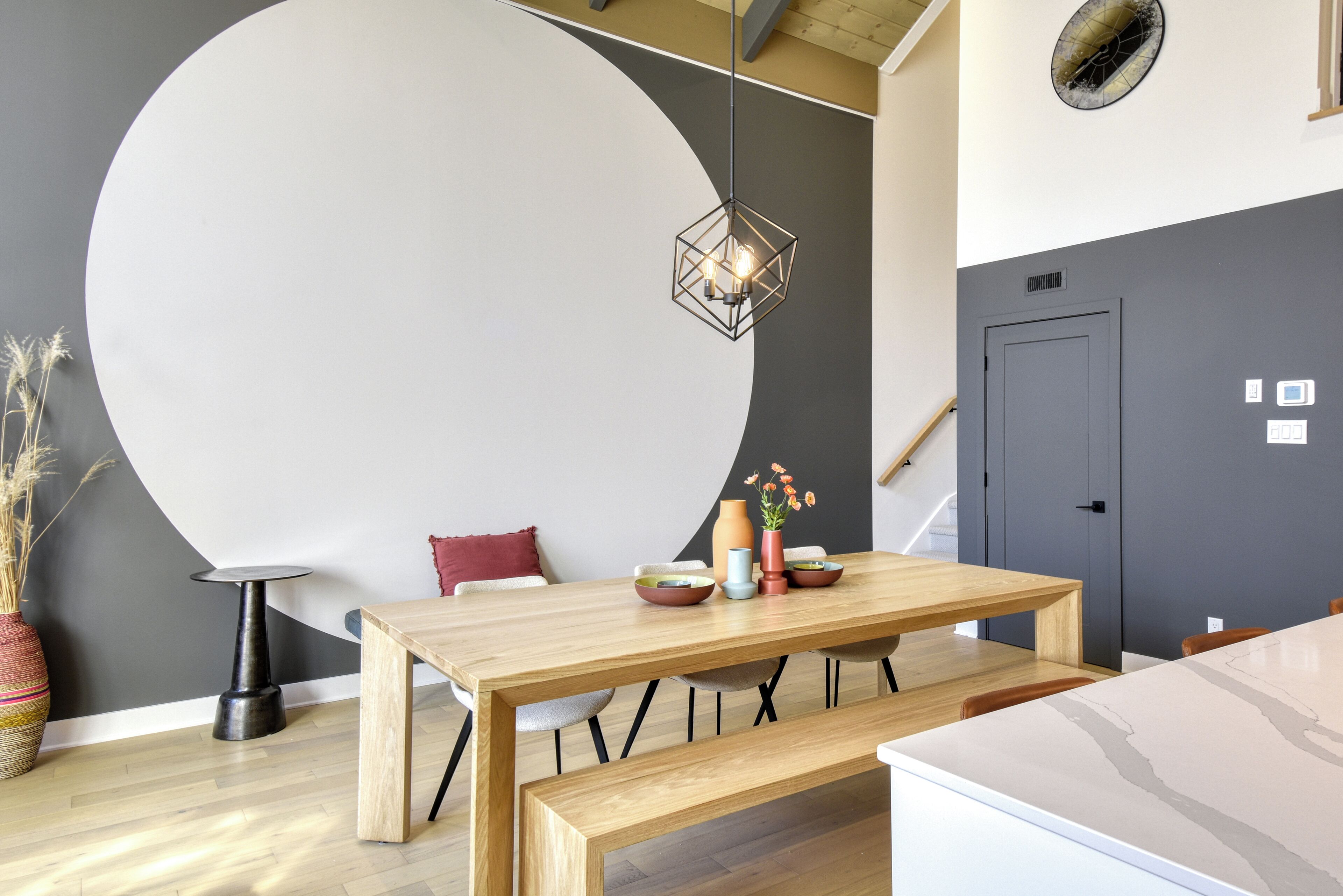 A modern dining area with a large round table, a hanging light fixture, and a minimalist decor.