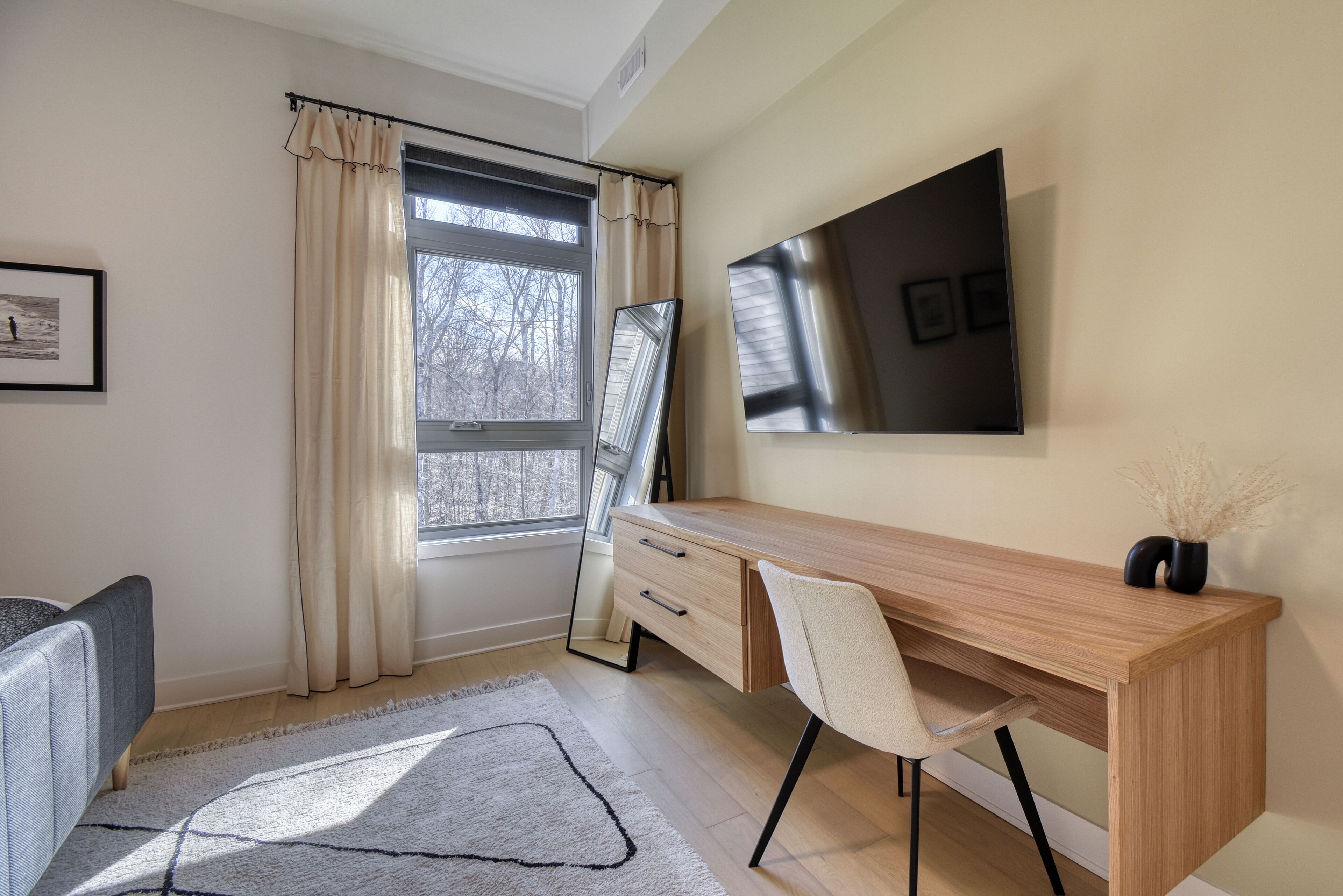 A modern office space with a wooden desk, a chair, a large mirror, and a window with curtains.