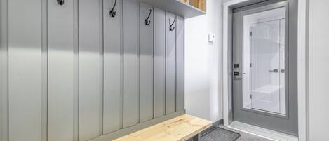 Ein moderner Umkleideraum mit grauen Schließfächern, einer Holzbank und einer Glastür.