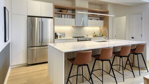 Una cocina moderna con una isla grande, electrodomésticos de acero inoxidable y taburetes de bar.