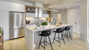 Una cocina moderna con una isla central, electrodomésticos de acero inoxidable y taburetes negros.