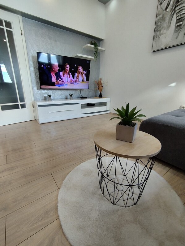 A modern living room with a flat-screen TV on a white entertainment unit, a round coffee table with a plant, and a grey sofa.
