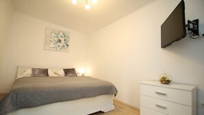 Ein Schlafzimmer mit Bett, Nachttischlampen, einem an der Wand befestigten Fernseher und einer Kommode.