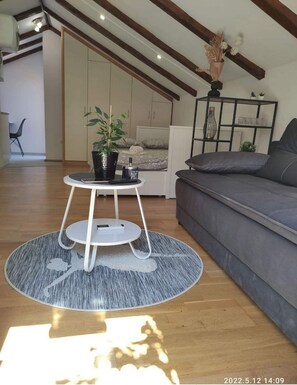 Relax in this stylish living space with a high ceiling, featuring a comfortable sofa, a coffee table, and a cozy bed.