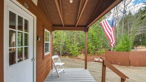 En træterrasse med en hvid stol, en dør med vinduer, og et amerikansk flag.