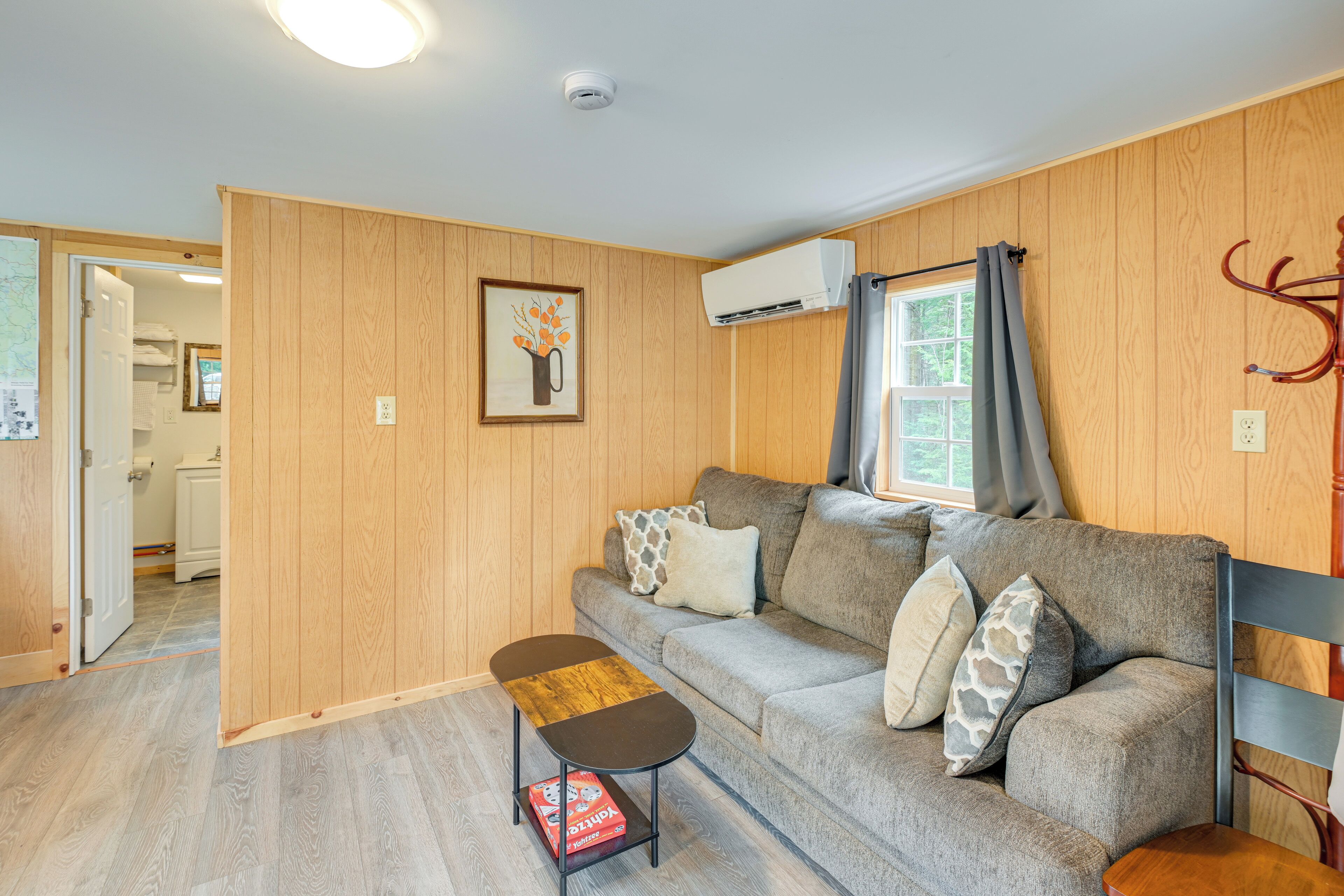 Een gezellige woonkamer met een grijze bank, een klein houten bijzettafeltje en een grijze fauteuil.