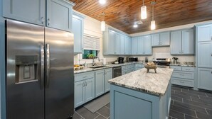Una cocina moderna con armarios azul claro, electrodomésticos de acero inoxidable y techo de madera.