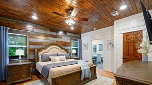 Un dormitorio con techo de madera, una cama grande con cabecera, una mesita de noche, un aparador y una puerta de madera.