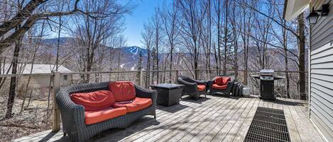 Una terraza con mobiliario exterior, una parrilla y vistas a montañas.