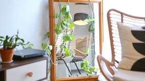 Ein Spiegel mit Holzrahmen, ein Blumentopf, ein Stuhl und eine Lampe.