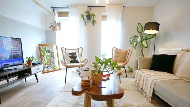Ein Wohnzimmer mit einer Couch, zwei Sessel, einem Couchtisch, einem Fernseher und Zimmerpflanzen.