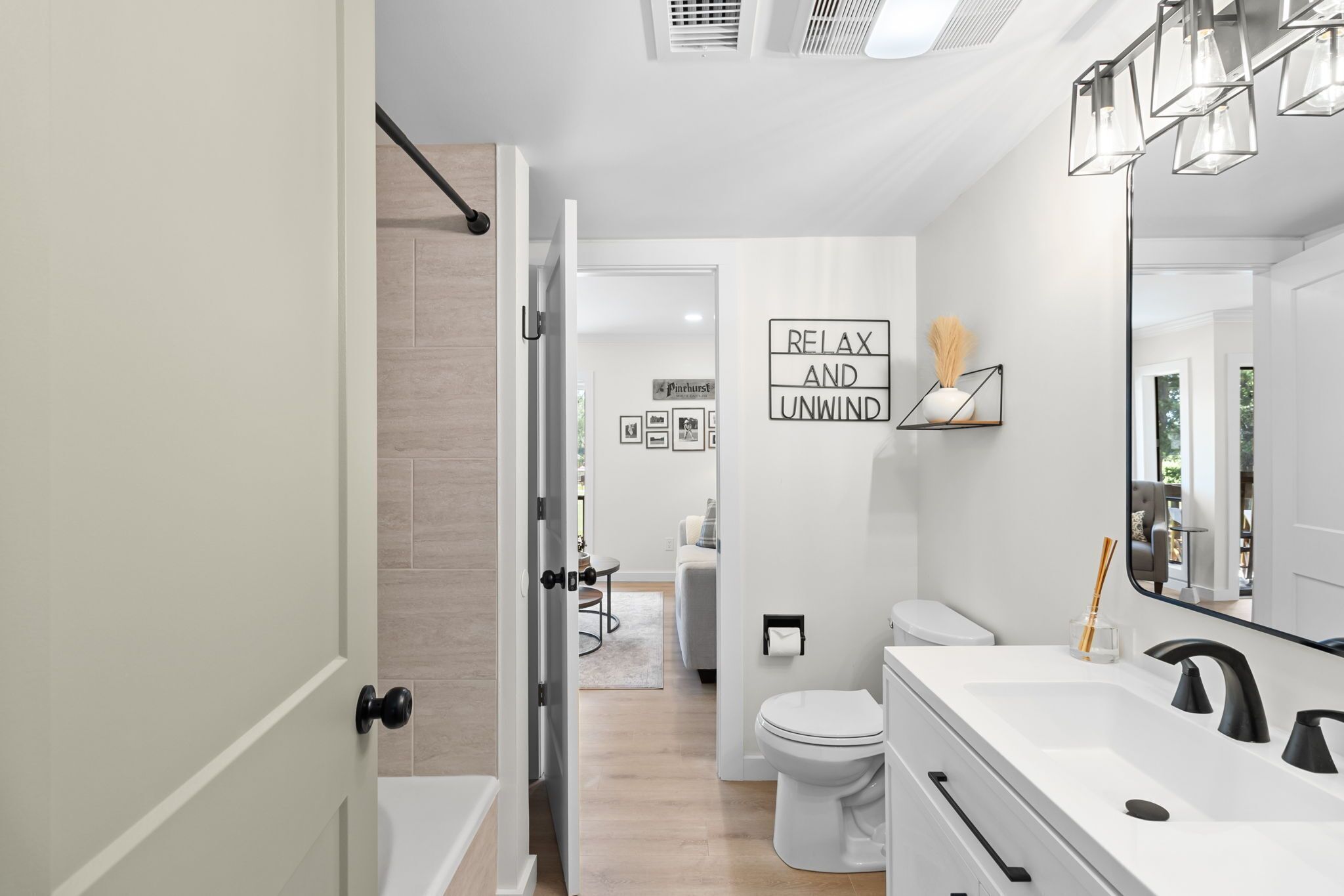A modern bathroom with a white sink, black faucet, and a mirror. There is a sign on the wall that says "RELAX AND UNWIND".