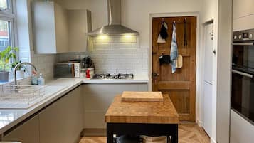 Een moderne keuken met witte kastjes, een gasfornuis, een magnetron en een houten kookeiland met snijplank.