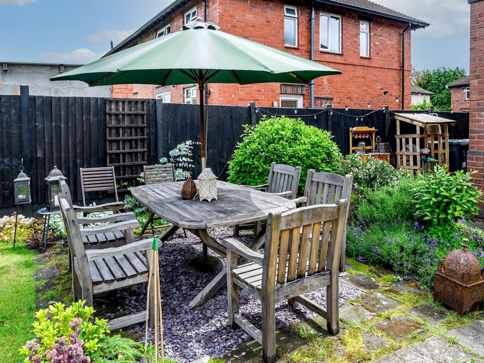 A wooden patio table with four chairs, an umbrella, and a lantern.