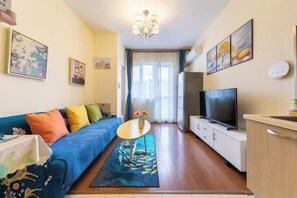 A compact living space with a sofa, a small table, a TV, and a kitchen area.