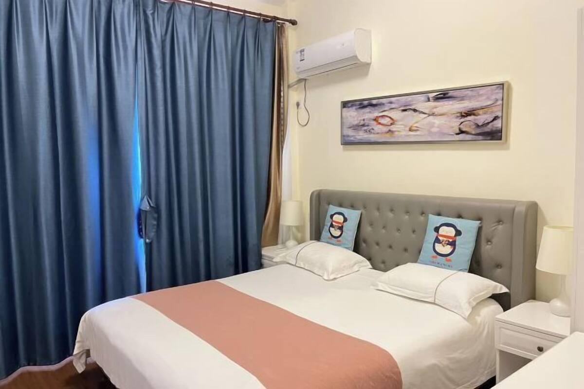 Une chambre d’hôtel avec un lit, une table de chevet, un climatiseur fixé au mur et un tableau.