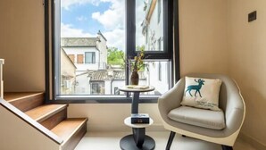 A modern room with a staircase, a small round table with a vase, and a chair with a decorative pillow. - Hongcun Lexian · Villa Hui-style Light Luxury Vacation Homestay (Nanhu) (Yi County)