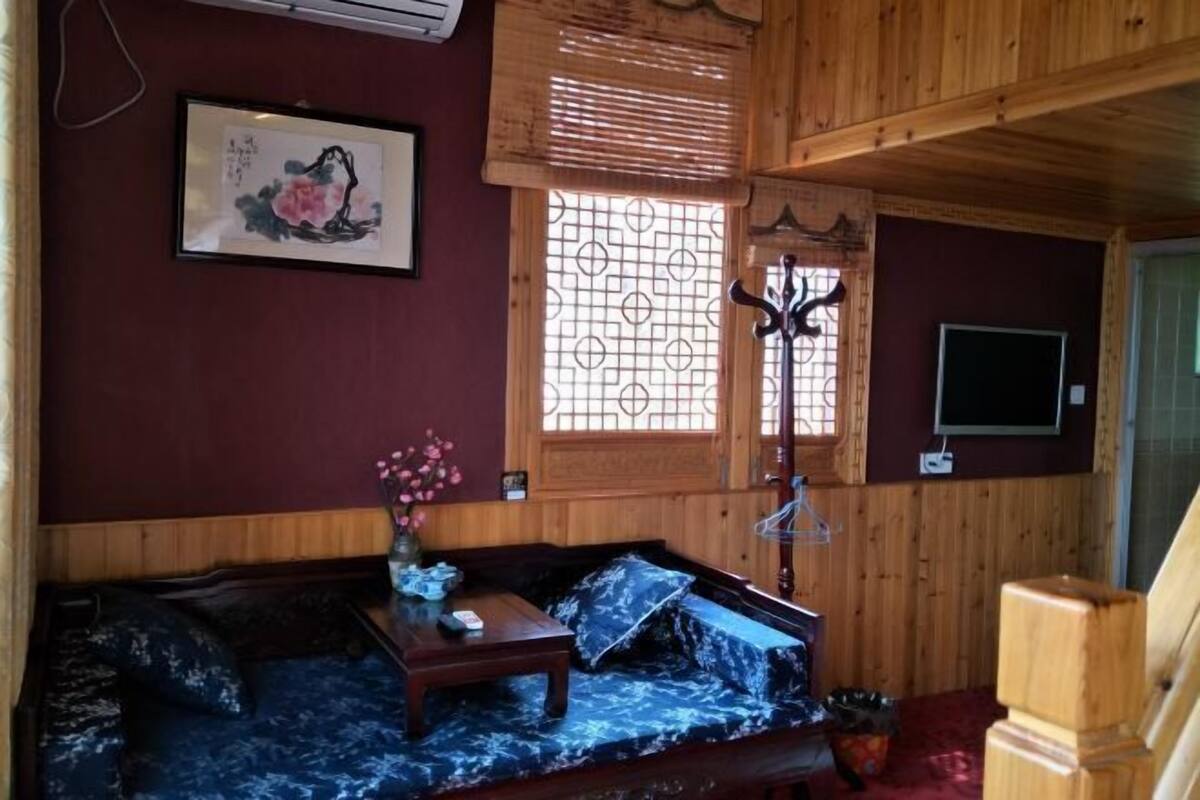 A wooden interior with a sofa, a small table, a TV, and a window with a decorative screen.