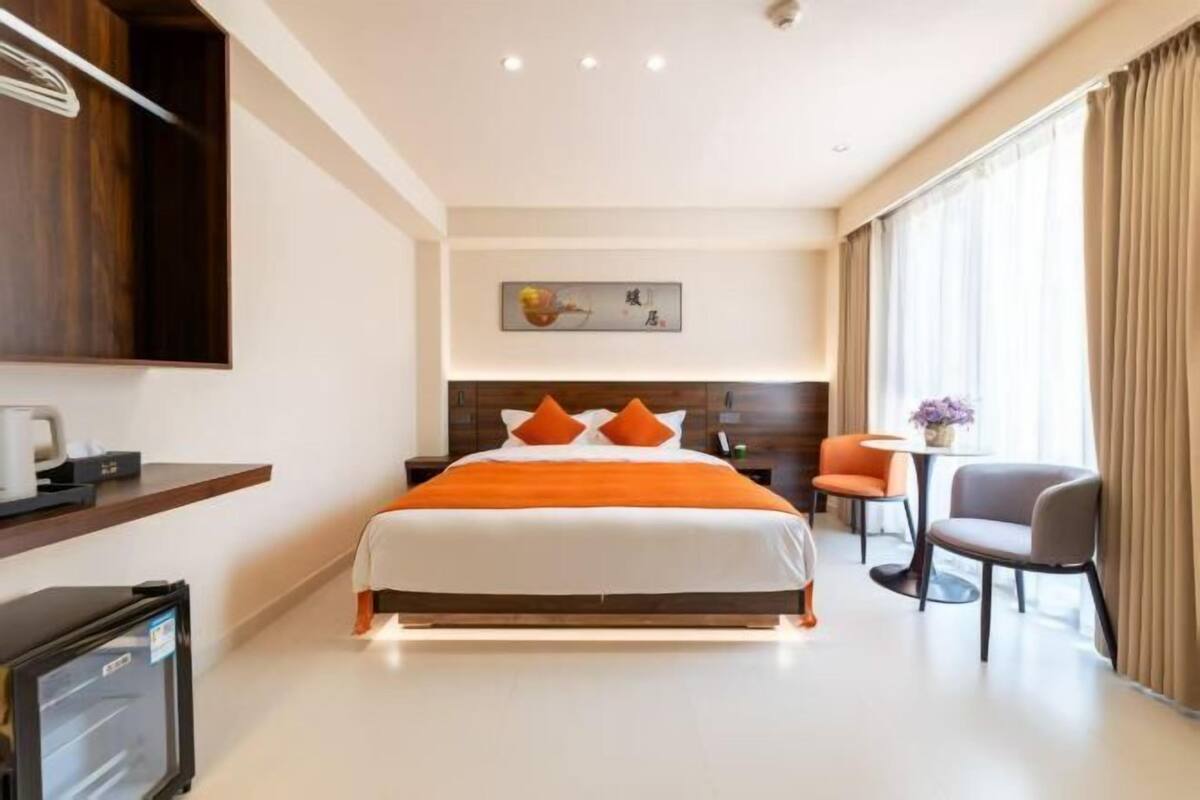 A hotel room with a large bed, a desk with a computer, a chair, and a small table with a vase.