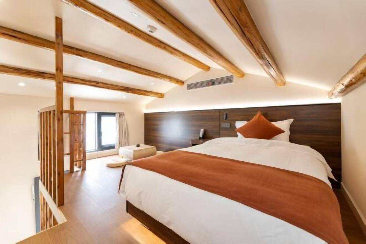 A bedroom with a large bed, wooden beams, a nightstand, and a window.