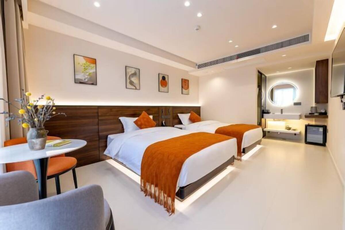 A modern hotel room with a large bed, a desk, and a small kitchenette.