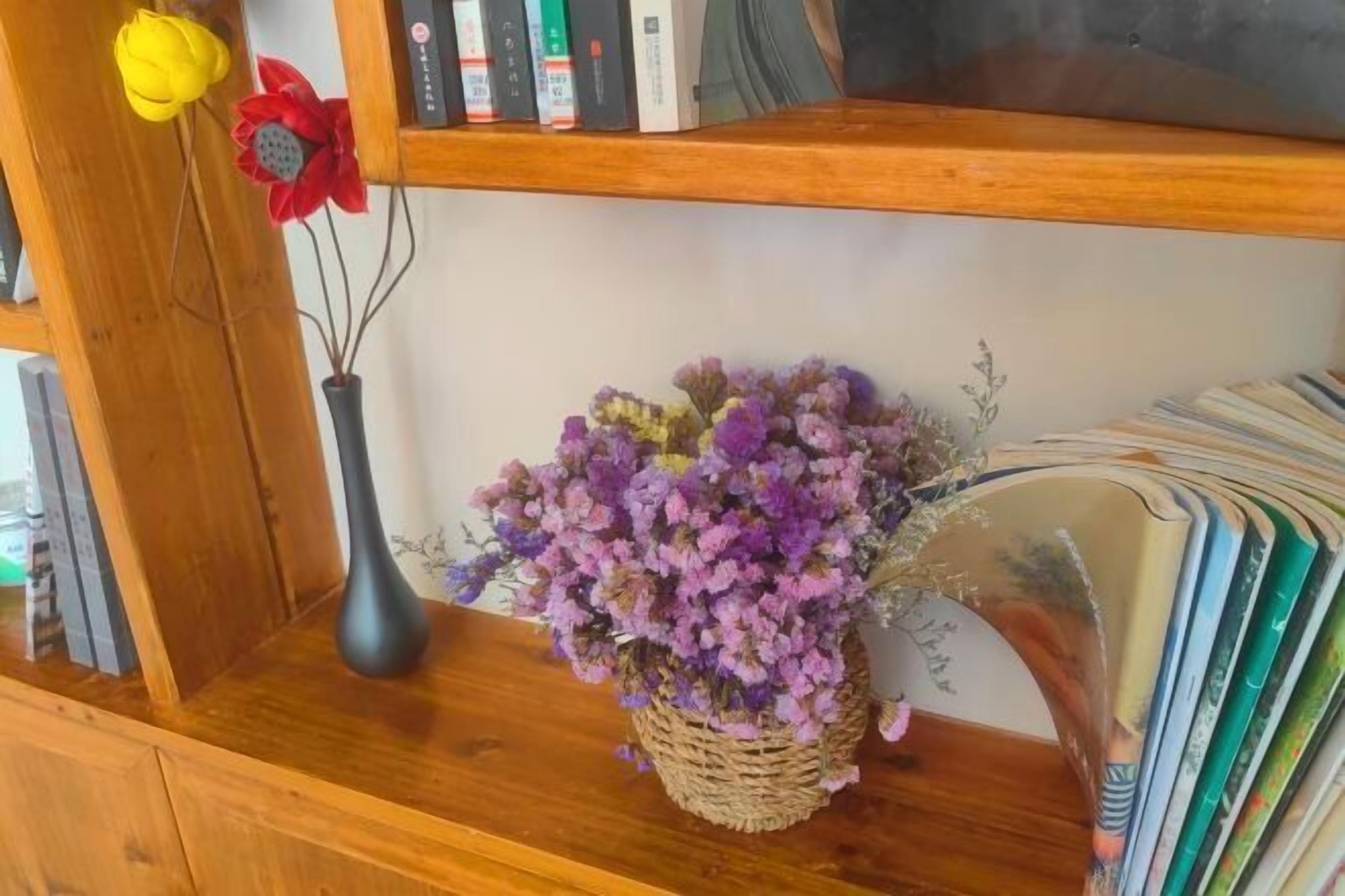 En hylla i trä med en vas med lila blommor, en gul blomma och en röd blomma.