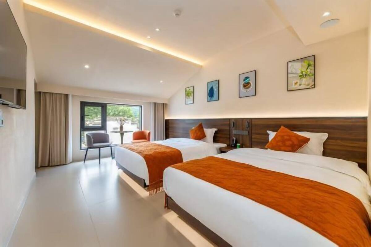 A hotel room with two beds, a large window, and a view of greenery outside.