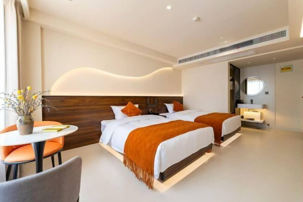A modern hotel room with two beds, a round table, and a small seating area.