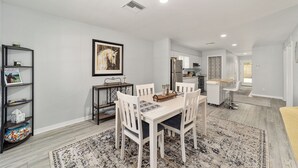 Un espace repas moderne avec une table et des chaises blanches, un tapis à motifs et un tableau encadré au mur.