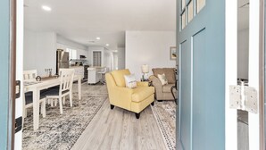 Un salon moderne avec un fauteuil jaune, un canapé beige et un coin repas comprenant des chaises blanches et une table.