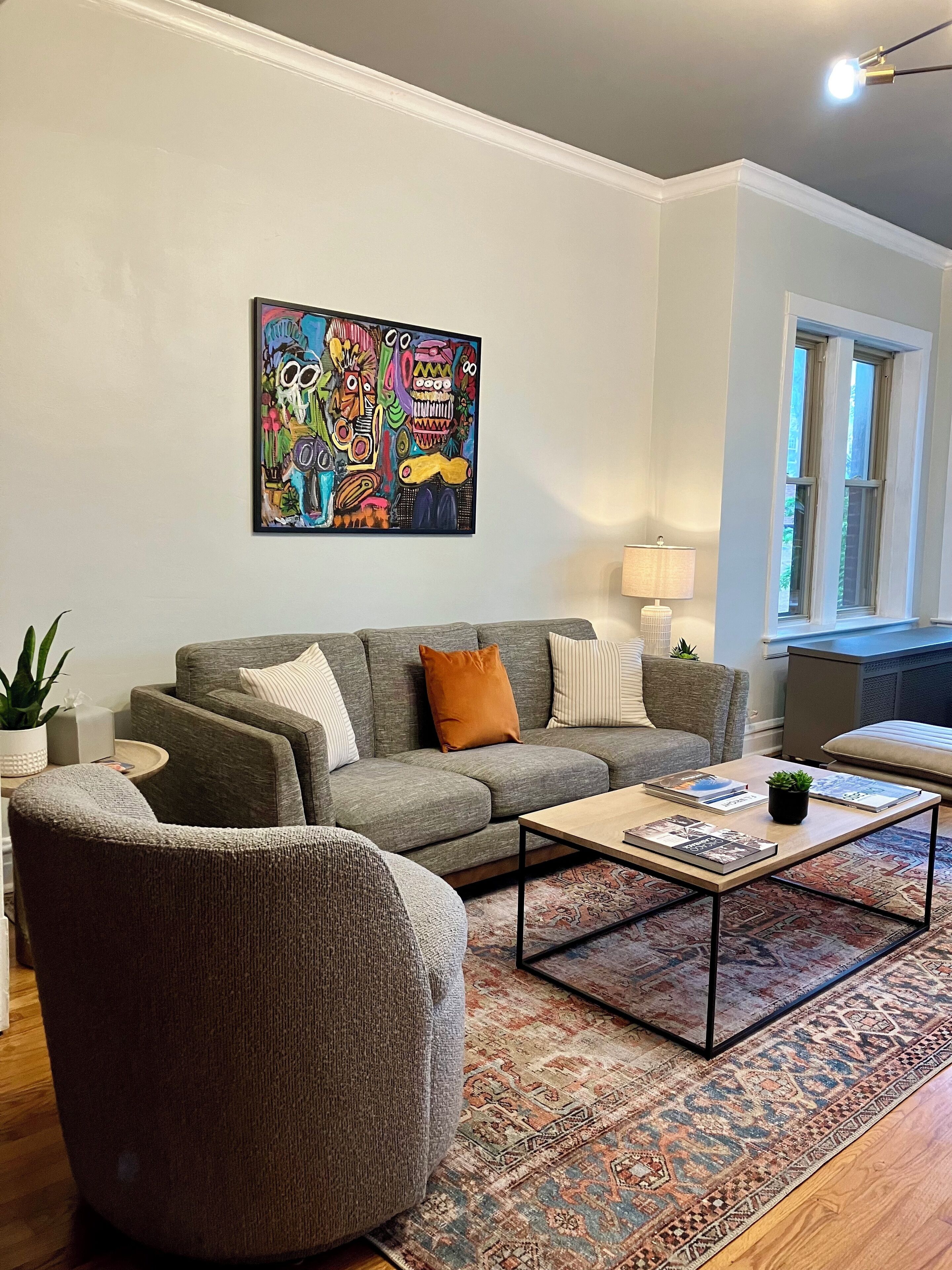 A living room with a grey sofa, a coffee table, and a colorful abstract painting on the wall.
