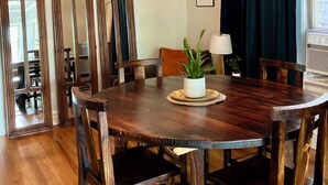 A dining room with a wooden table, chairs, and a chandelier. There are three arched mirrors on the wall and a window with curtains.