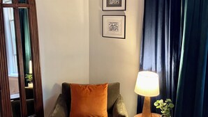 A room with a dark green armchair, a wooden side table with a lamp, and a mirror with a wooden frame.