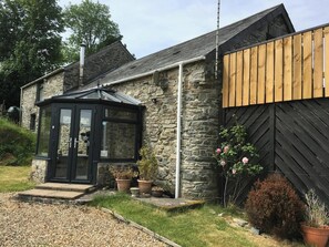 Une maison en pierre avec une véranda, une clôture en bois et des plantes en pot.