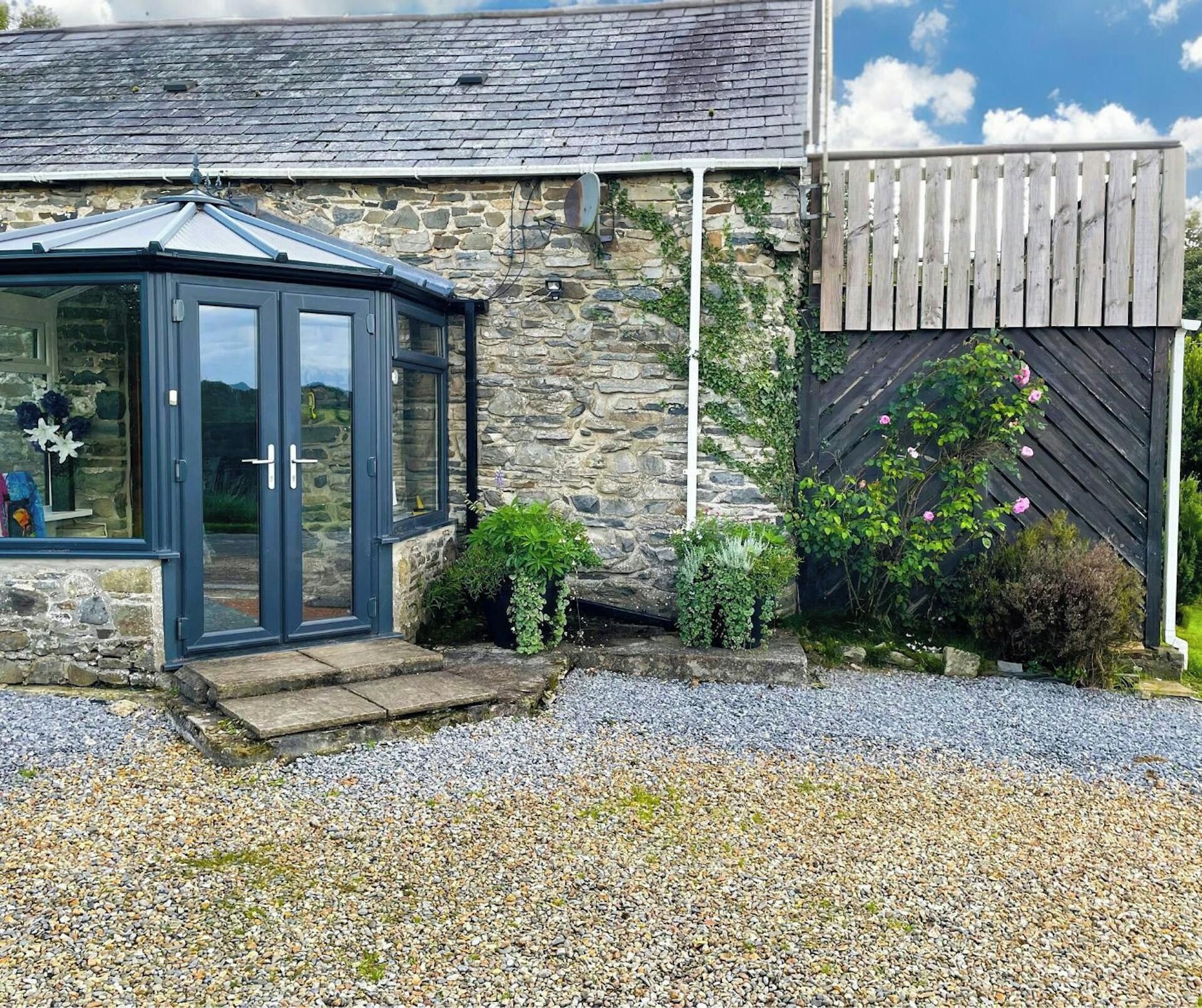A stone building with a conservatory, gravel driveway, and a wooden fence.