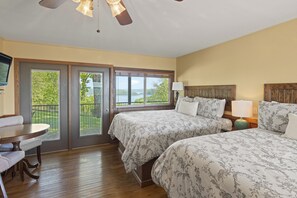 A bedroom with two beds, a dining table, and a view of a lake. - Roadrunner Inn and Log Cabins (Eureka Springs)