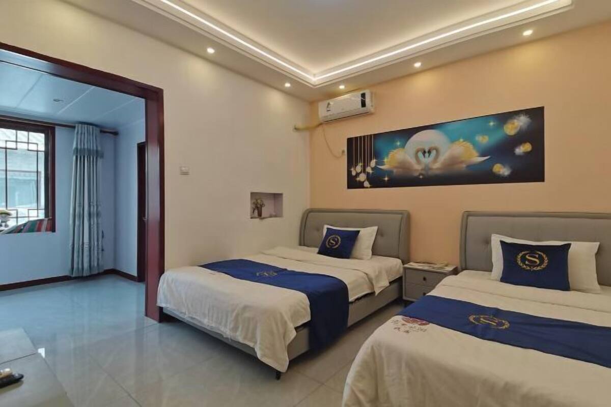 A hotel room with two beds, a painting on the wall, and an air conditioning unit.