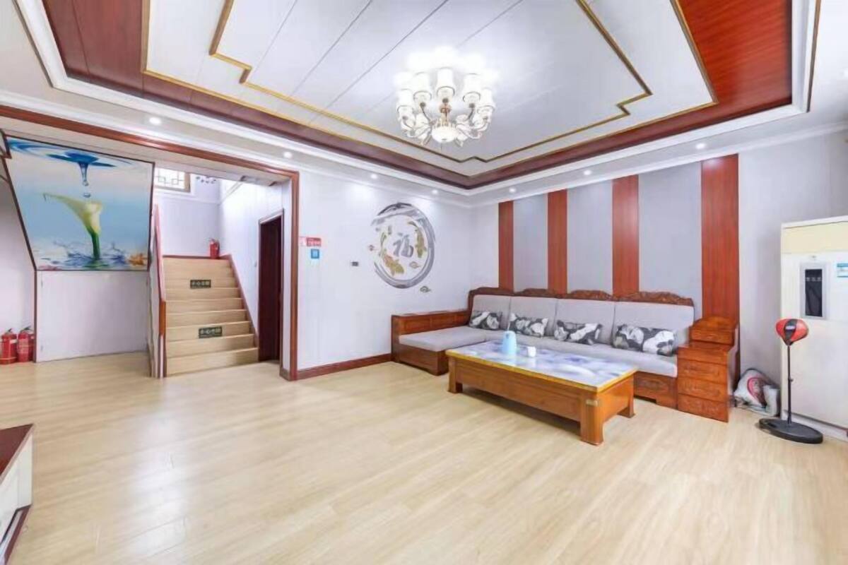 A spacious living room with a sofa, coffee table, and a chandelier. There is a staircase leading to another room and a wall with a circular design.