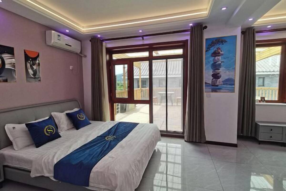 A bedroom with a bed, a window, a painting, and an air conditioning unit.