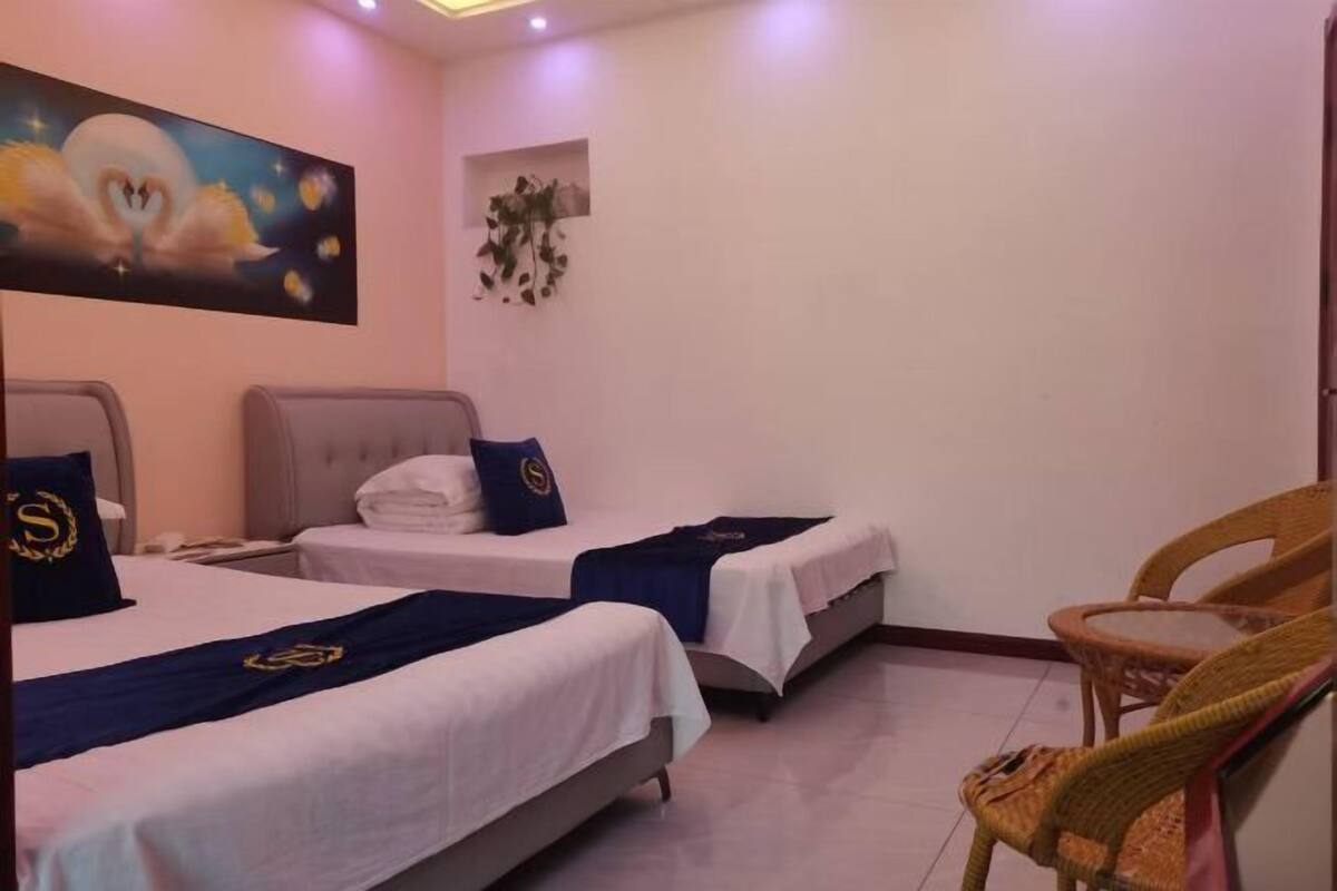 A hotel room with two beds, a small table, and a wicker chair.