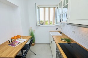Ett modernt kök med vita skåp, en träbänkskiva, en svart spis och ett fönster med gardiner.
