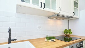 A modern kitchen with white cabinets, a wooden countertop, a black induction cooktop, and a stainless steel oven.