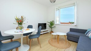 A modern living room with a dining area, a grey sofa, a TV, and a large window with a view.
