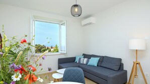 A modern living room with a grey sofa, a small white table, and a dining table with a plate of croissants.