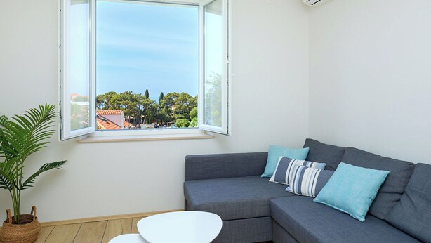 A modern living room with a grey sofa, a small white table, and a large window with an open view of a cityscape.