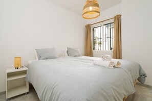 Un dormitorio con cama, mesita de noche, lámpara y ventana con cortinas.