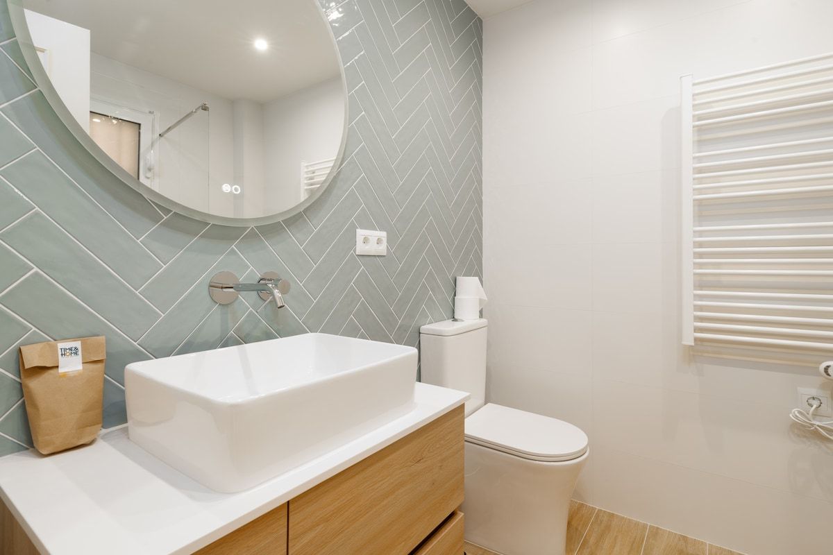 Een badkamer met een wit wastafel, houten opbergmeubel, toilet en spiegel.